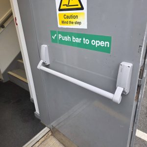 Fire exit push bar fitted to metal fire exit door displaying green push bar to open signage 